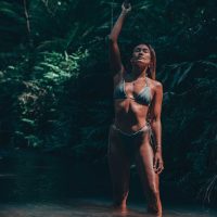 Lifestyle Photography of a woman standing in a river in the jungle with a waterfall behind her.