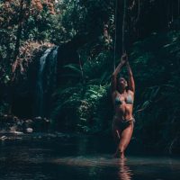 Lifestyle Photography of a woman standing in a river in the jungle with a waterfall behind her.