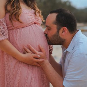 Couple posing for their maternity photos. Dad kissing the baby belly